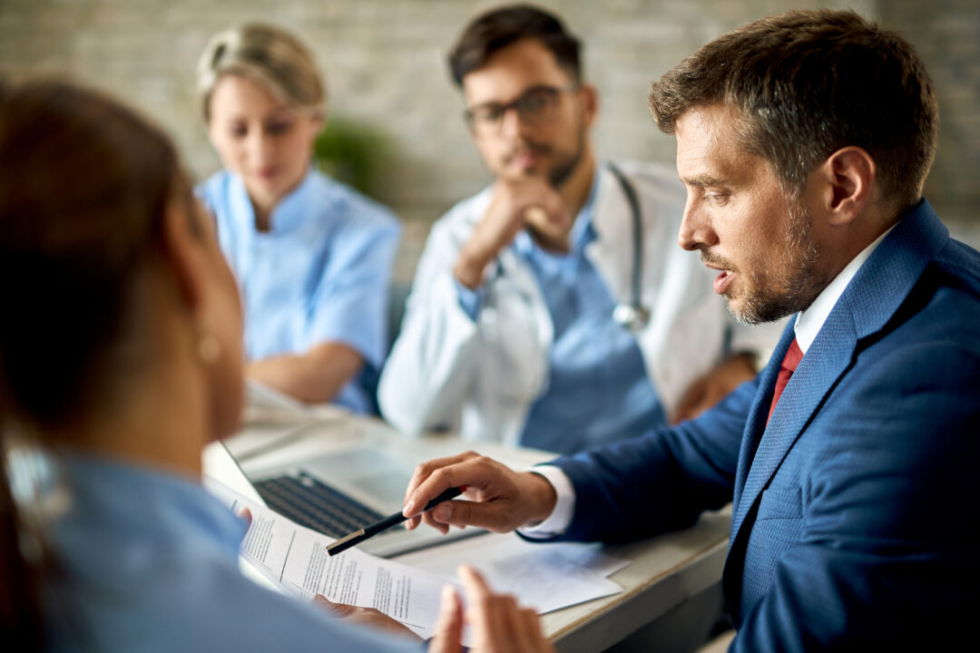 Businessman cooperating with doctors while going through reports Mid adult businessman and healthcare workers analyzing documents during a meeting in the office.